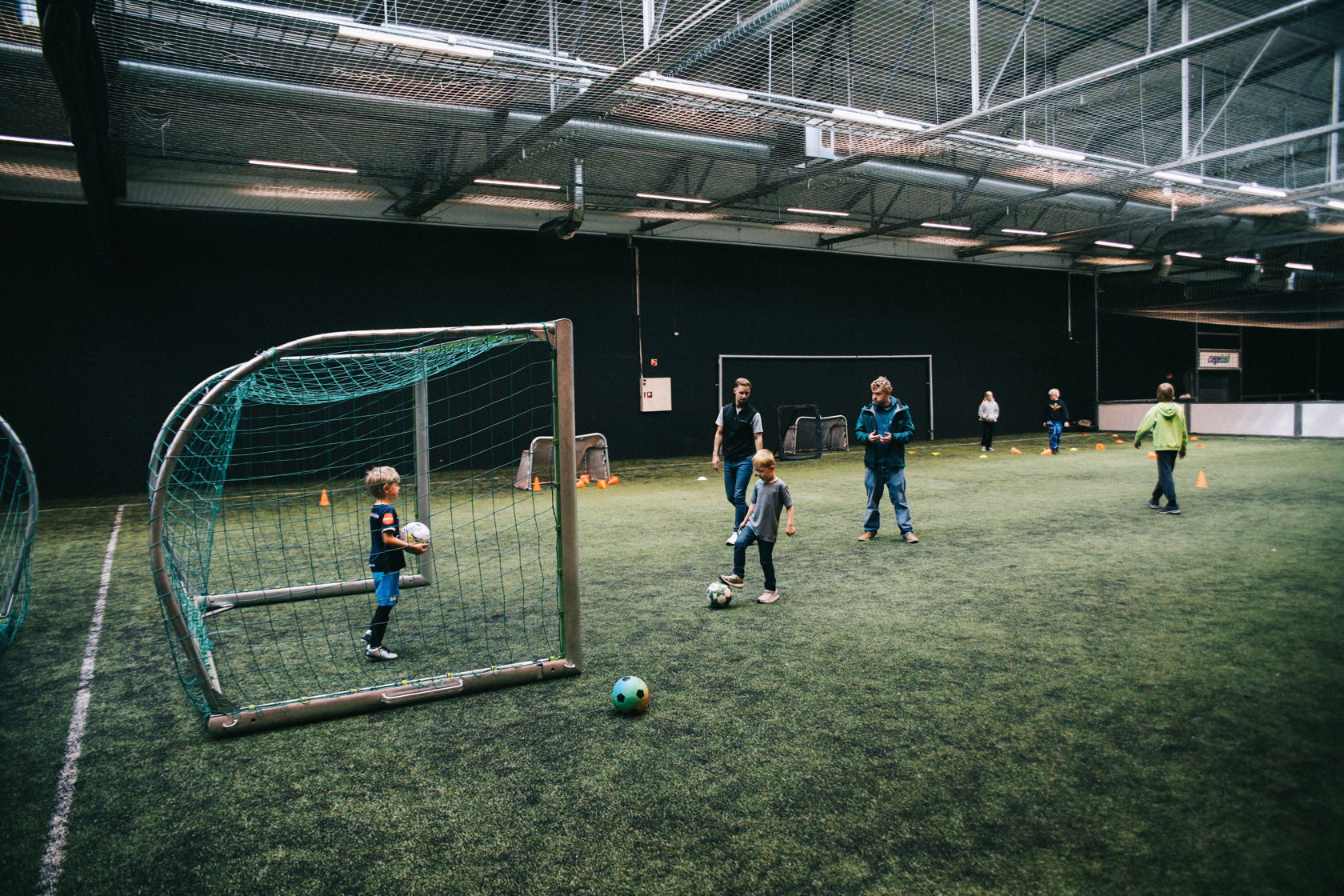 Barn og voksne spiller fotball på innendørs kunstgressbane